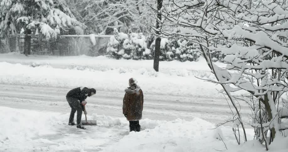 Man shoveling snow from driveway while another person watches