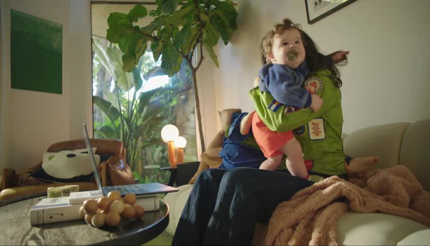 A mother laughs while fussing with two kids on a couch in a living room