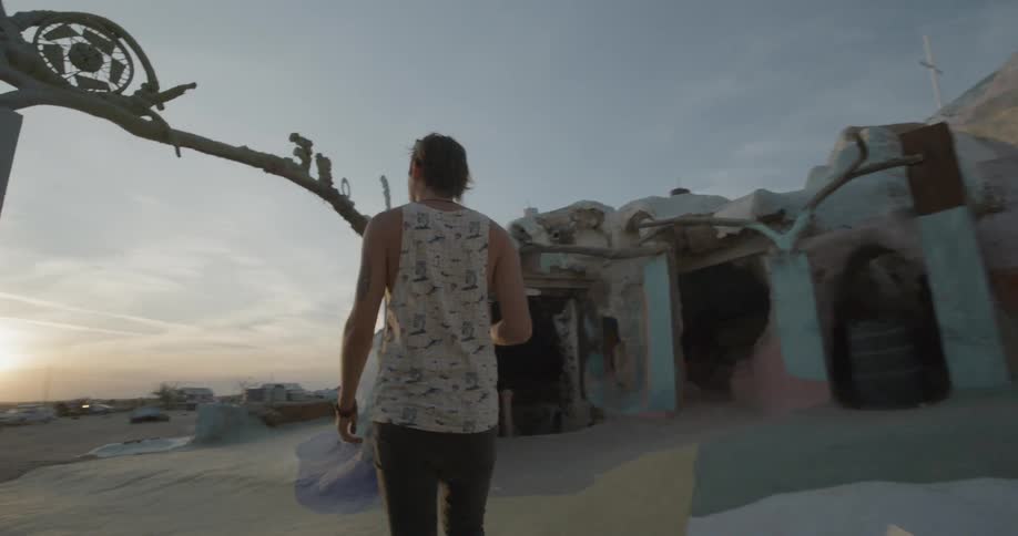 A man walks out of a cave towards the desert at sunset