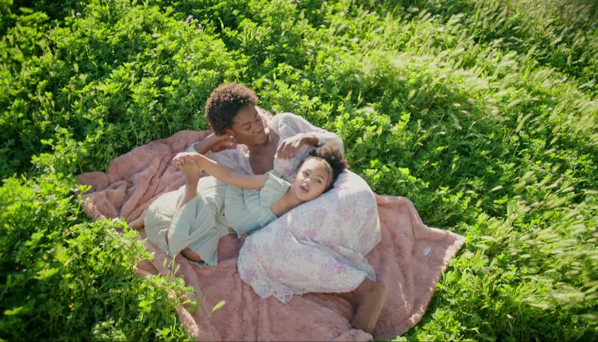 A mother and her daughter lie on a large towel on a grassy area