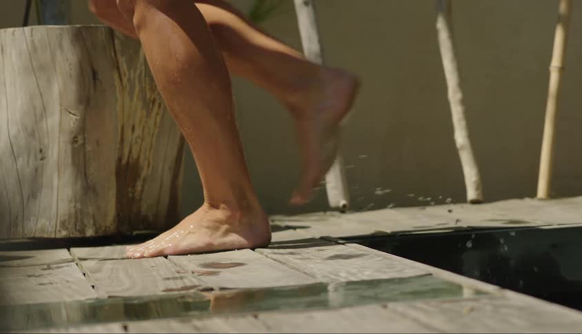 A closeup of a persons bare feet walking out of a pool on a wooden surface