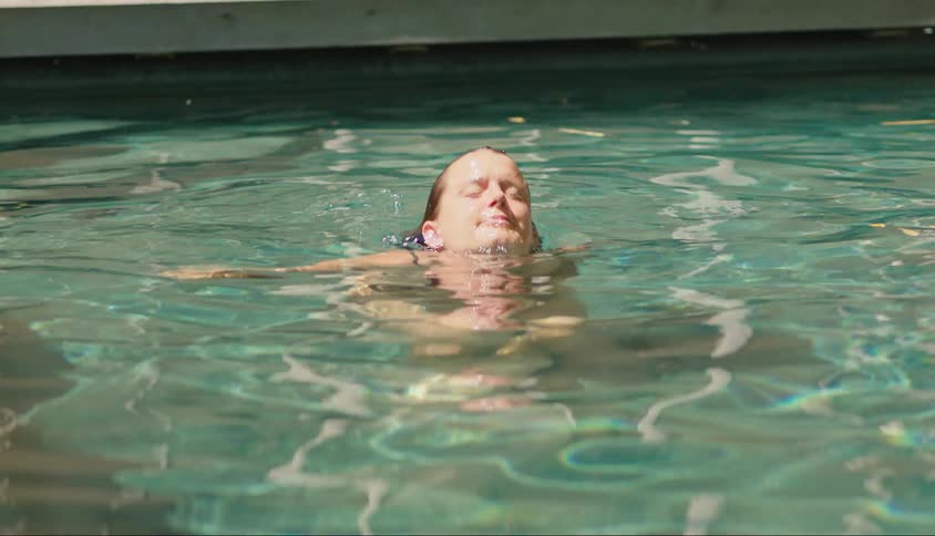 Woman swimming in a pool with sun glare