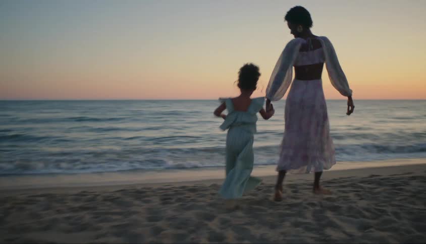 Mother and daughter running hand in hand on the beach in the late afternoon
