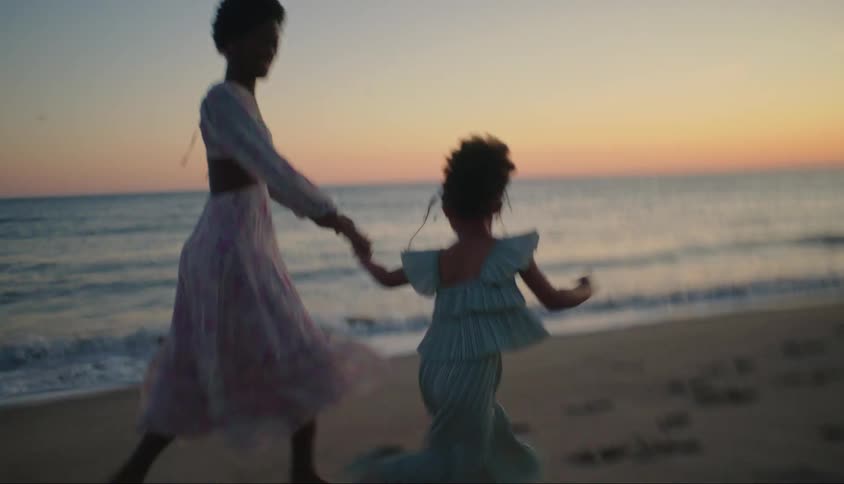 Mother running hand in hand with her little daughter on the beach in the late afternoon