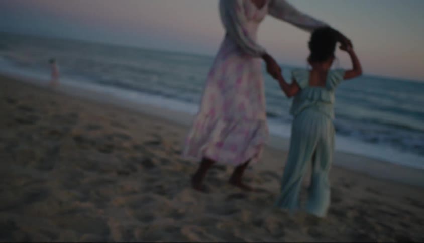 Mother holding hands with her little daughter spinning around playing in the sand on the beach in the late afternoon