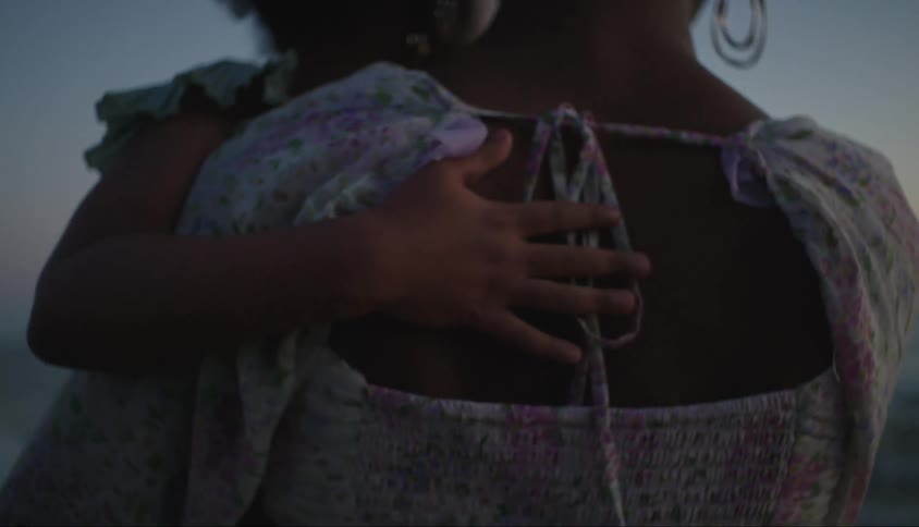 A little girls hand on her mothers lap resting on her back in a beach setting in the late afternoon
