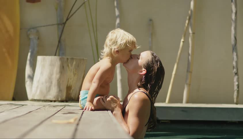 Mother in the pool giving a kiss to her little son