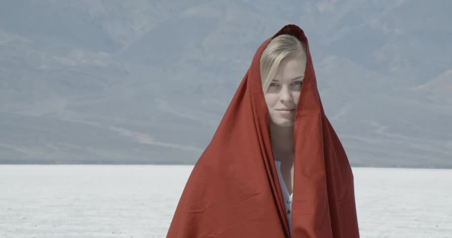 Woman standing before mountains wearing a red blanket over her head