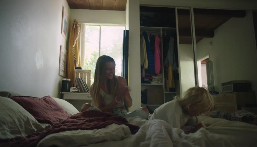 A young boy jumps on the bed his mother laughs