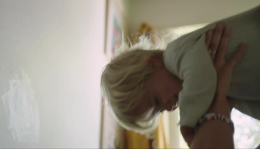 Mother lying in bed holding her little son up with her hands