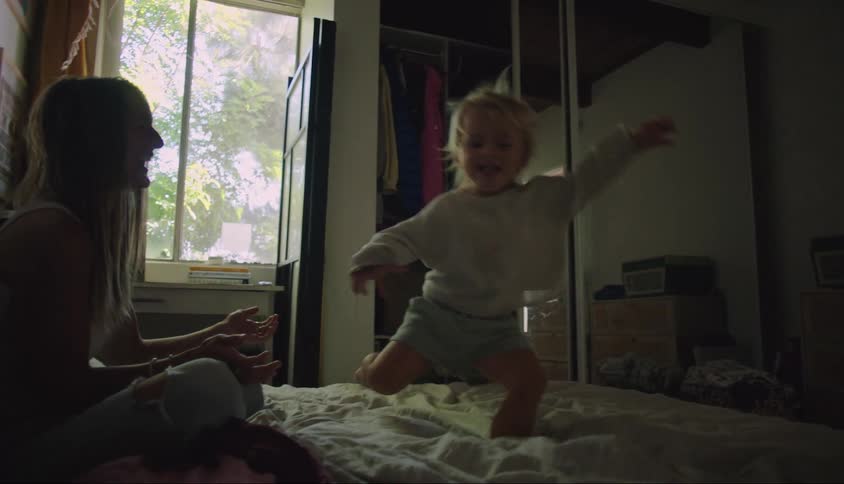 Child playing running on the bed with his mother sitting next to him