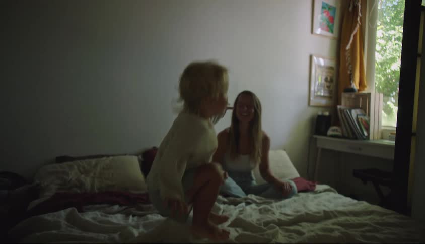 A little blond boy jumping on a bed and a woman applauding