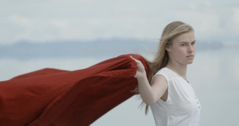 A woman holding a red blanket behind her as the winds blows it