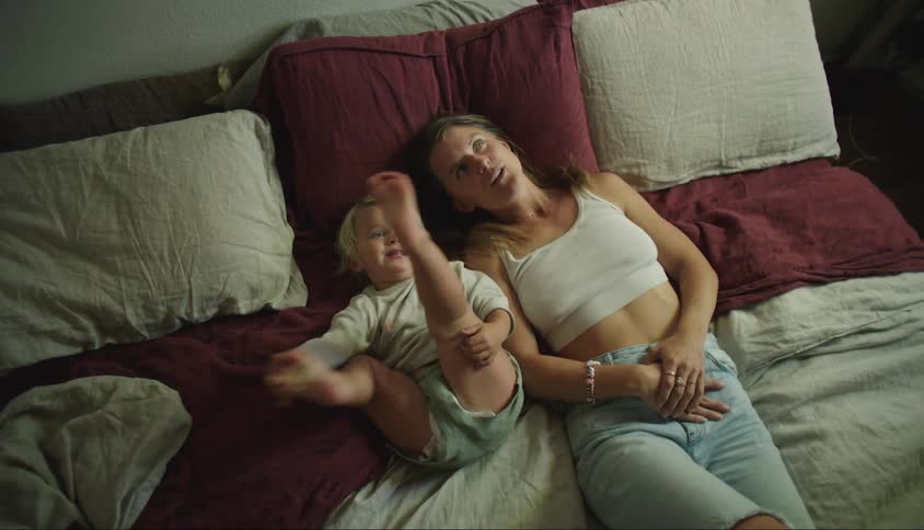 A woman and her little son are lying in bed and smiling while pointing up and talking