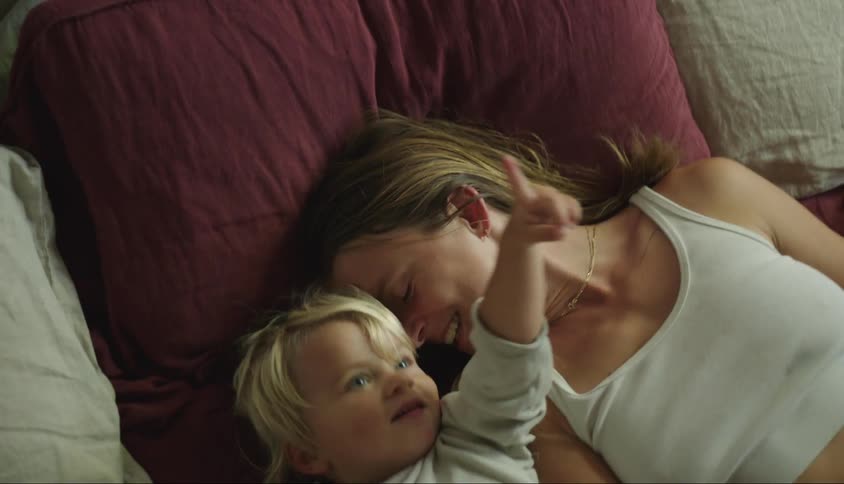 A mother and her son clown around together while lying in bed