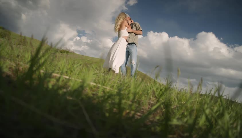 A man kisses a pregnant woman while outdoors in a field