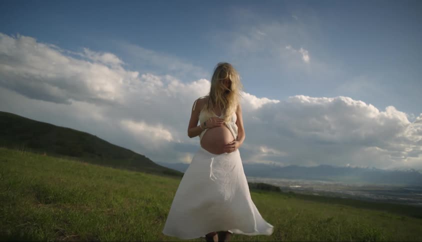 Woman in white dress walking on a hill and holding her hand on her pregnant belly