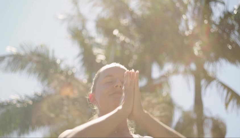A teenager strikes a yoga stretching pose near palm trees outside