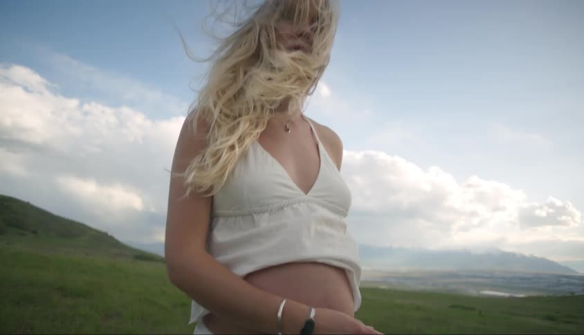Pregnant blonde woman with bare stomach walking in a field
