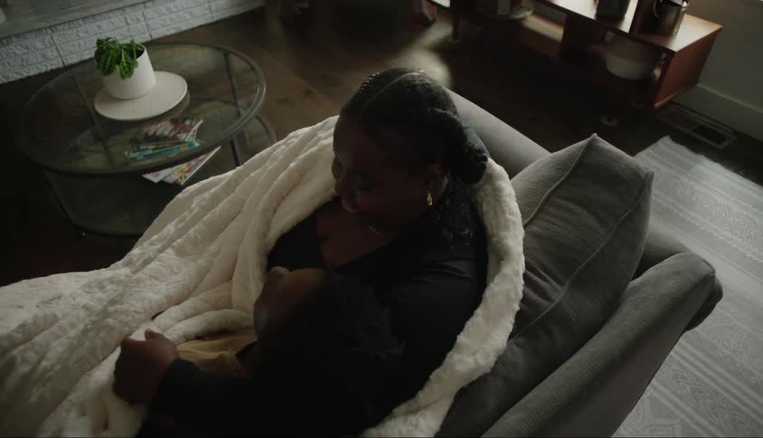 A mother embraces her child while wrapped in a blanket and sitting on a couch