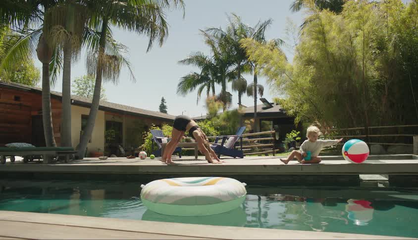Woman stretching her body with her child by her side in a relaxing outdoor environment with a swimming pool