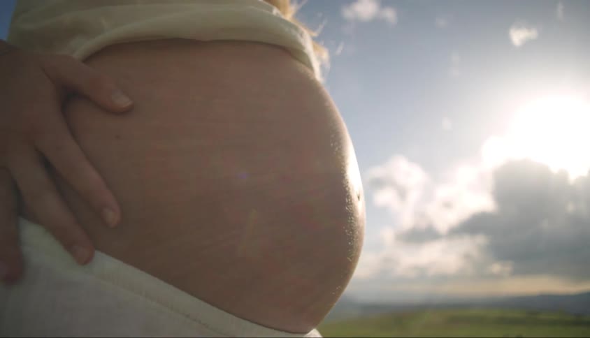 Closeup of a pregnant woman with her belly showing in a field