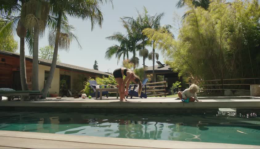 A teenage girl stretches by a pool as her little brother plays nearby