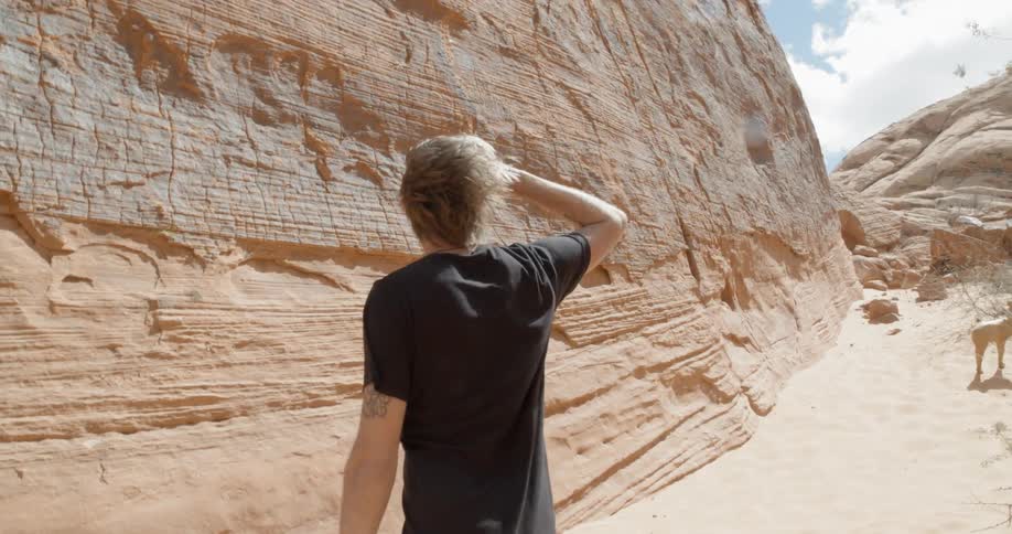 Man looking around at the base of a large rock on a windy day