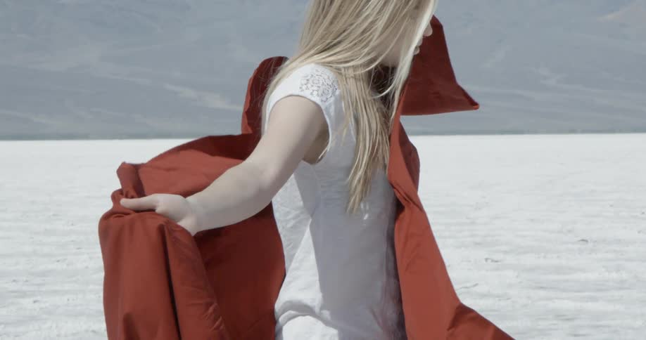 Blonde woman in a white top holding a large red cloth behind her with her arms spread wide outdoors