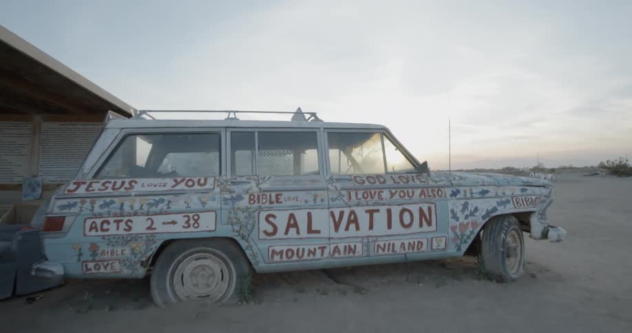 A car with writing all over it is parked outside in a desert