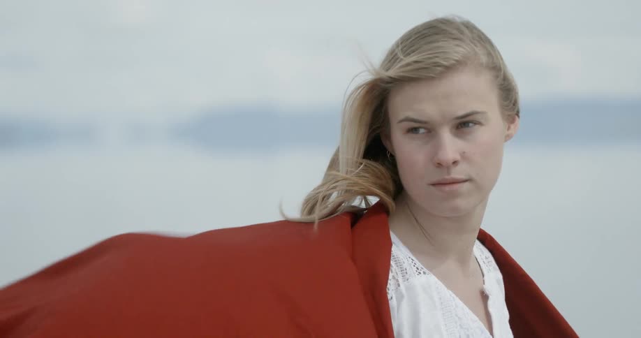 Woman standing outside wearing red shawl that is flowing in the wind