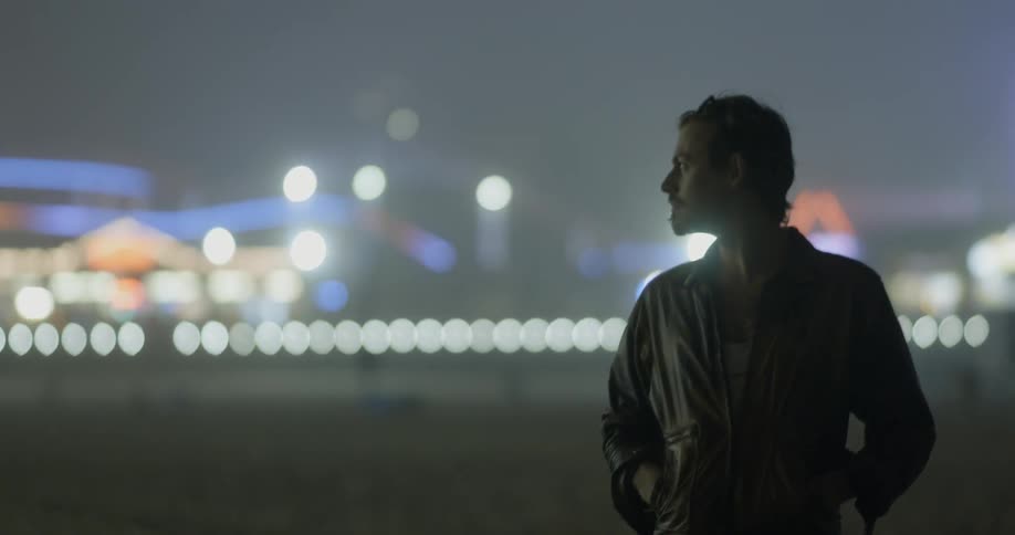 A man standing in a field outside a carnival at night