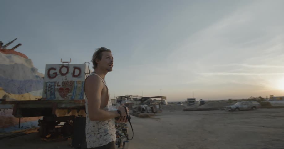 A man holding a camera looks around the desert ahead at sunset