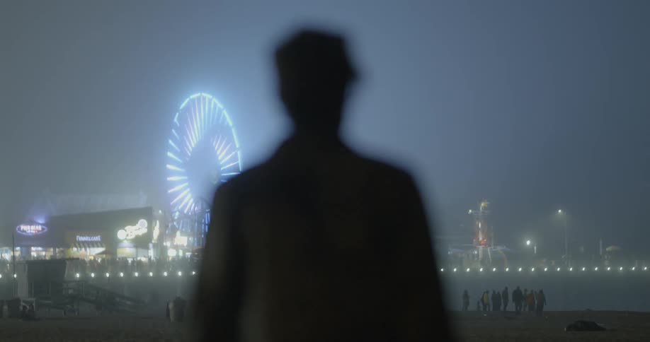 A man walks on the beach towards a carnival at night