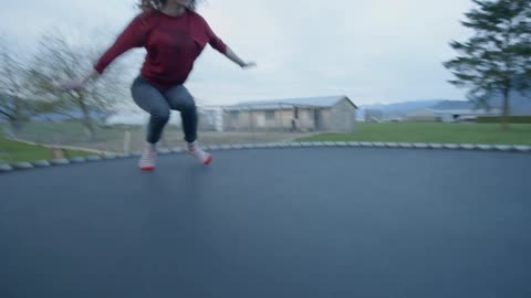 Woman performing a backflip on an outdoors trampoline on a fall day