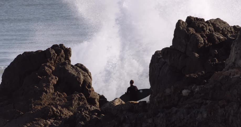 A large wave crashes against the shore near the surfer