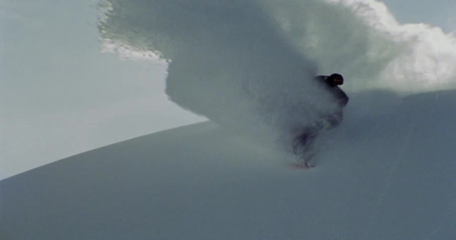 A person snowboarding and skids and kicks up a lot of snow