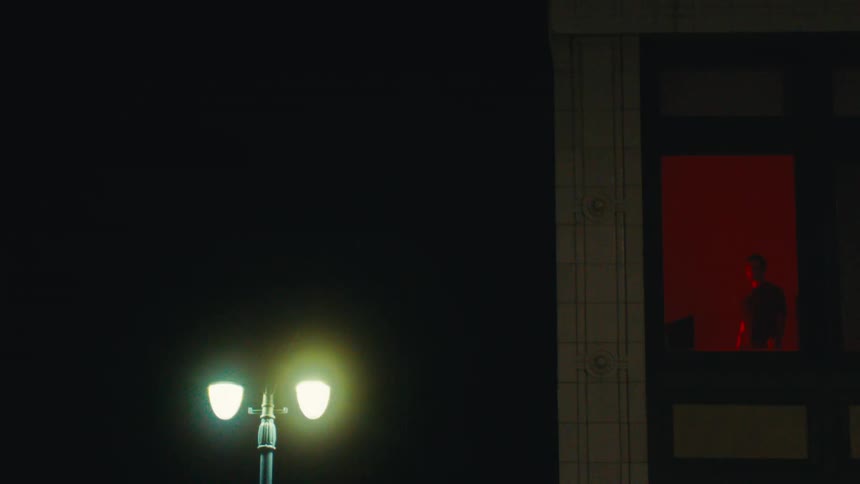 Window of a building with a man in a room with red light at night