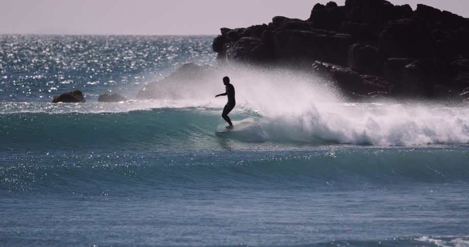 The silhouette of a man is seen as he surfs on a small wave