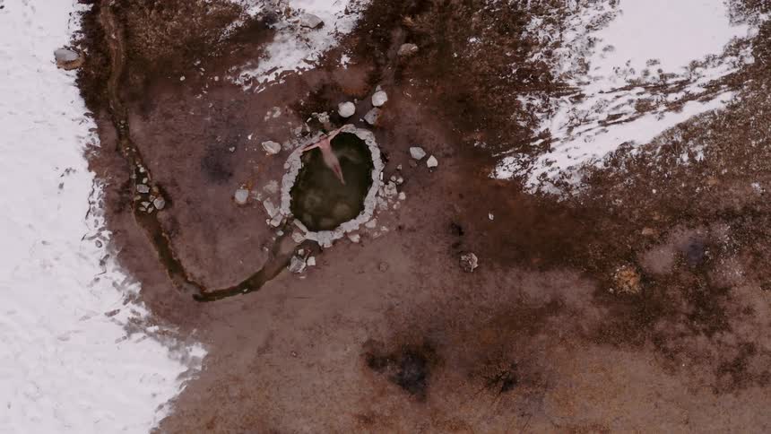 Aerial panorama of a person in a hole with hot springs surrounded by snow