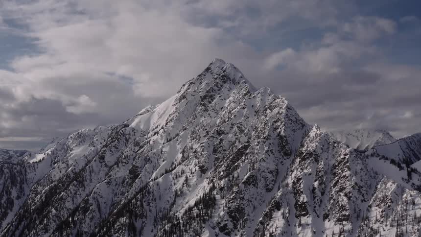 Aerial of snowcapped mountain peaks with white clouds in the background