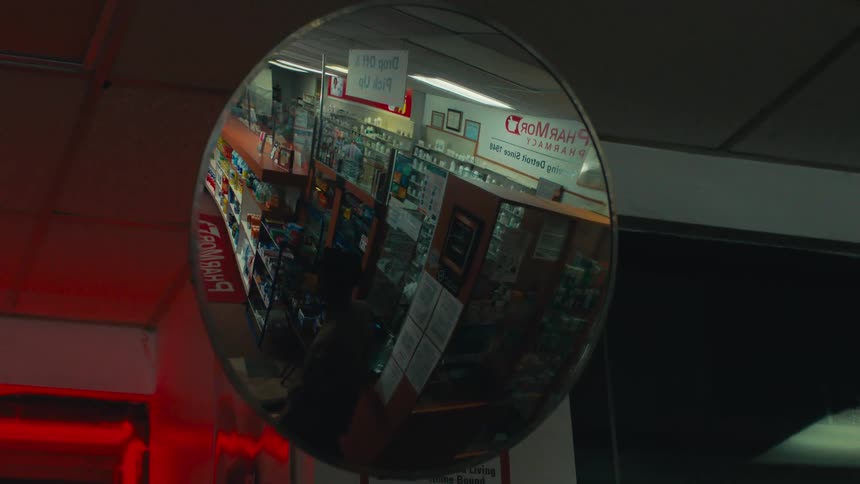 A round mirror in a store reflecting a person walking down one of the aisles