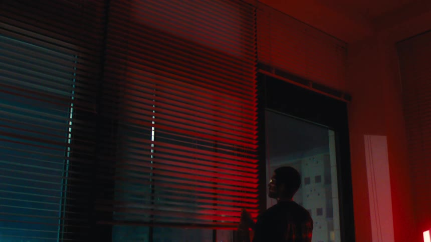 A person has their back turned and is closing an internal curtain and they are receiving a strong red light coming from the side