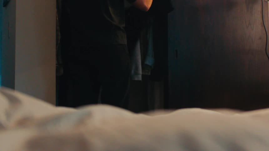 A man rummages through a closet and throws a shirt on a bed
