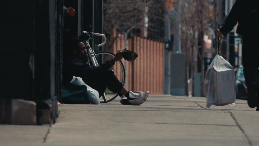 Discouraged man sitting on the street sidewalk asking for money with his cap