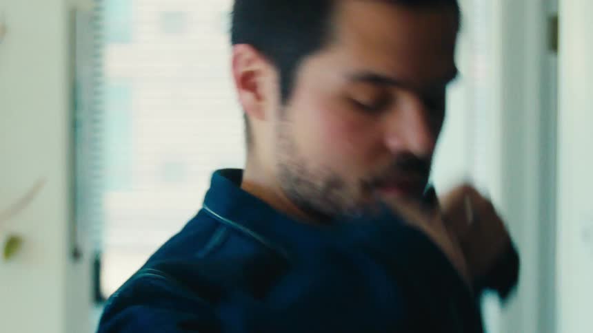 Bearded man picking up a denim jacket and putting it on