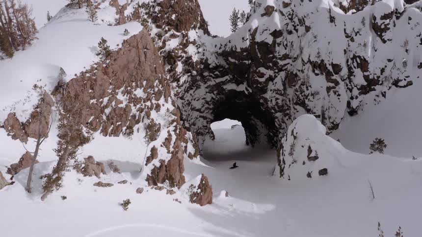 A person snowboards through a hole in a mountain