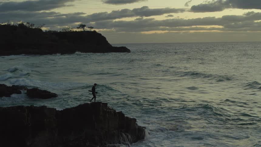Silhouette of a person walking on a rocky cliff by the sea