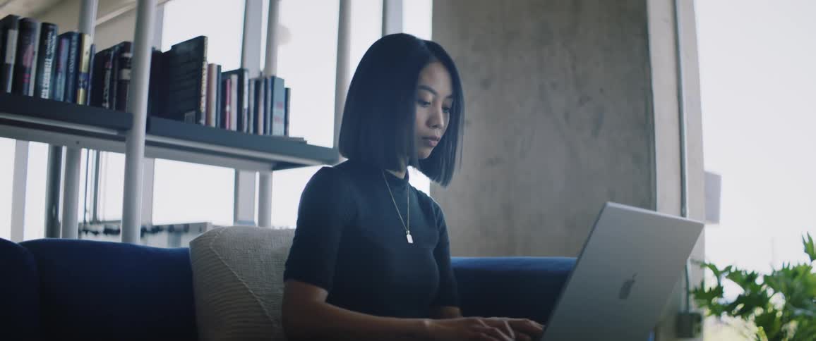 Woman sitting near window and bookcase works on her laptop