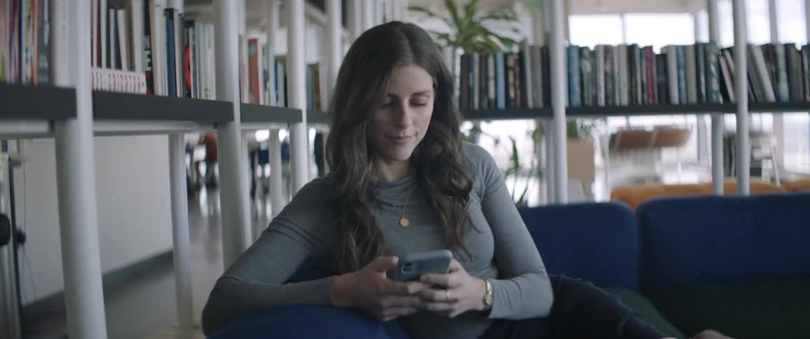 Woman sitting in an armchair using her cell phone while there are bookshelves around her